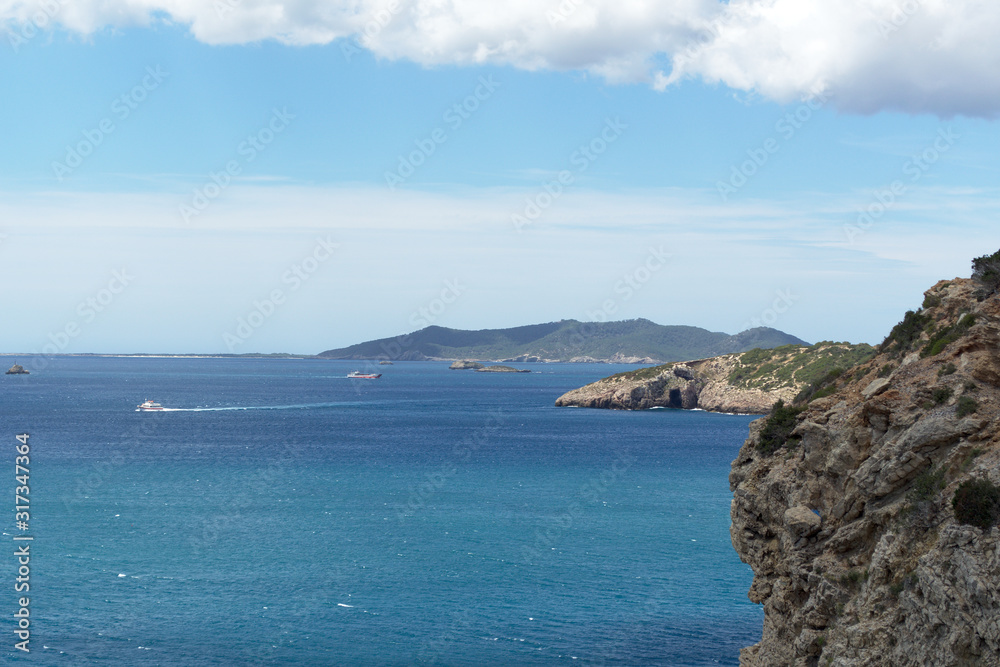Rocky sea coast with clean blue water, cloudy sky and city view. Ibiza island, Spain Rocky sea coast with clean blue water, cloudy sky and city view. Ibiza island, Spain