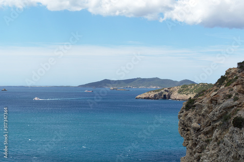 Rocky sea coast with clean blue water, cloudy sky and city view. Ibiza island, Spain