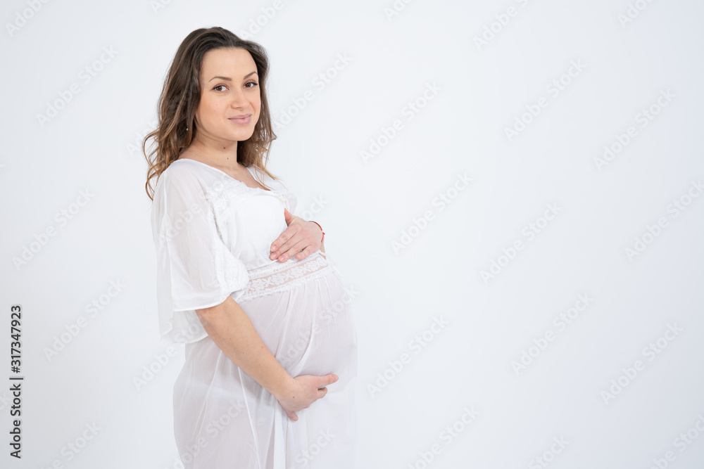 Side view portrait of the attractive bunette pregnant girl with loose hair, dressed in white underwear and holds her hands on her swollen belly, isolated over white background, copyspace for your text Side view portrait of the attractive bunette pregnant girl with loose hair, dressed in white underwear and holds her hands on her swollen belly, isolated over white background, copyspace for your text
