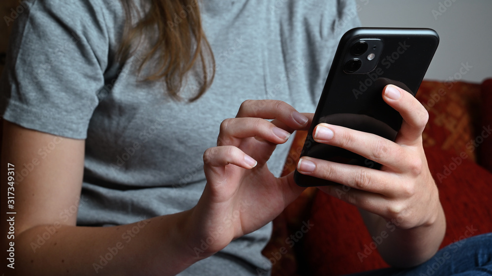 Fototapeta premium Young woman or girl using mobile phone at home on sofa and texting a message in social media app.