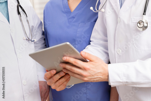 Doctor in medical team discussing patient report at tablet computer in hospital