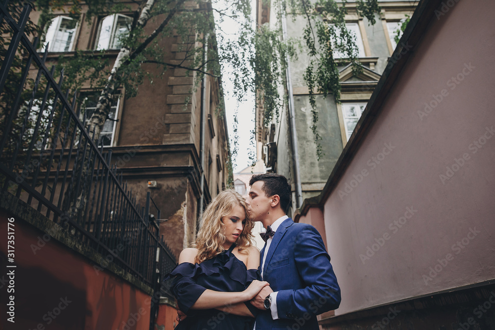 Stylish couple embracing and kissing in european city street. Sensual passionate moment. Fashionable man and woman in love gently hugging. Valentines day
