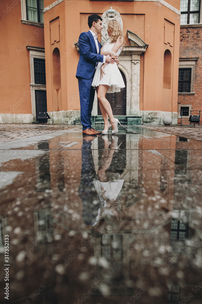 Stylish couple dancing in european city street on background of old architecture and reflection in water. Fashionable man and woman in love dancing. Traveling together in Europe