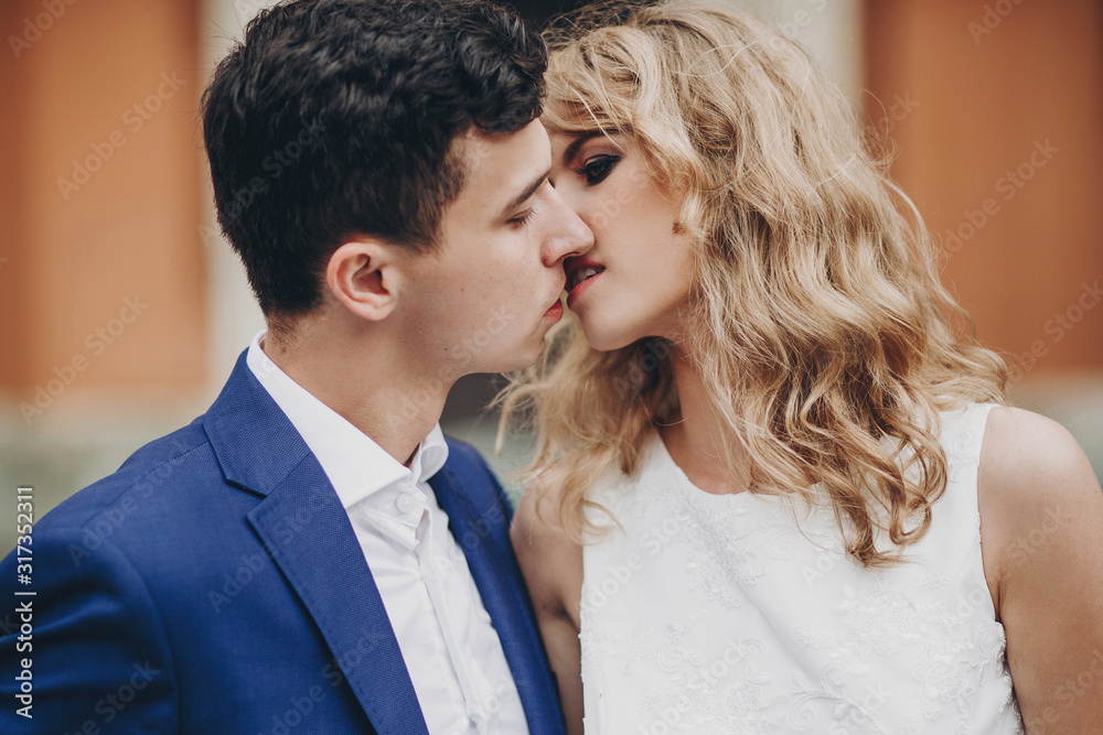 Stylish couple embracing and kissing in european city street. Sensual passionate moment. Fashionable bride and groom in love gently hugging. Valentines day Stylish couple embracing and kissing in european city street. Sensual passionate moment. Fashionable bride and groom in love gently hugging. Valentines day