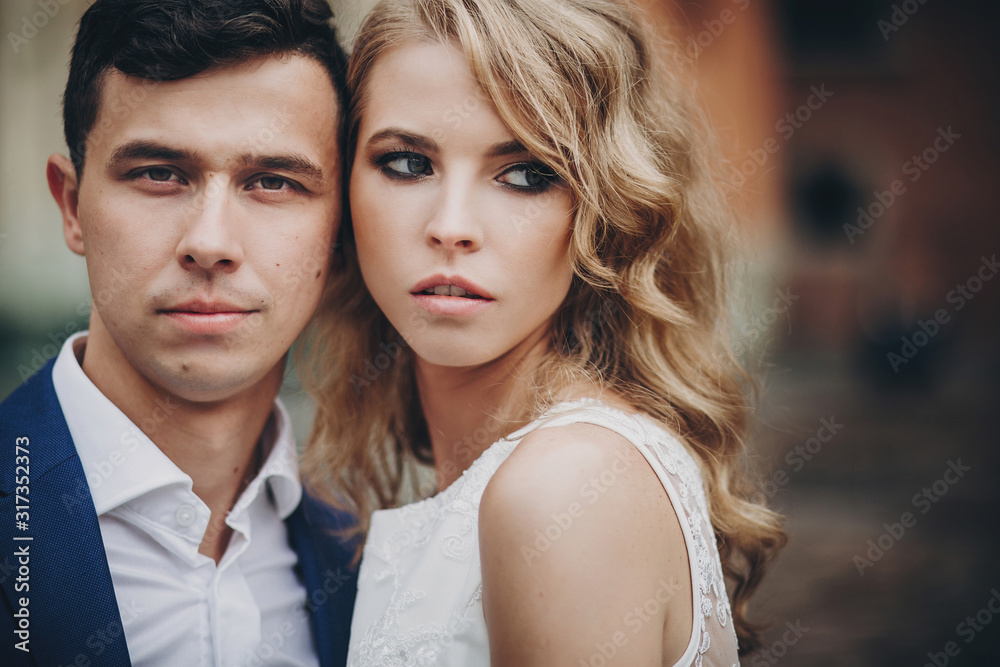 Fototapeta premium Portrait of stylish couple embracing in european city street. Sensual romantic moment. Fashionable bride and groom in love posing with passionate look. Valentines day
