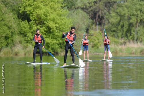 Canvas-taulu group of holiday maker doing stand up paddle board lesson