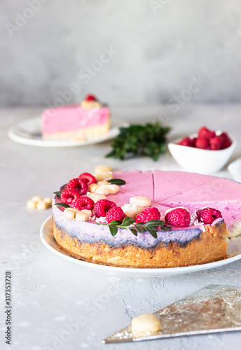 Piece of raspberry cream mousse cake (no baked cheesecake) decorated with fresh raspberries, mini cookies and coconut flakes on light grey background.