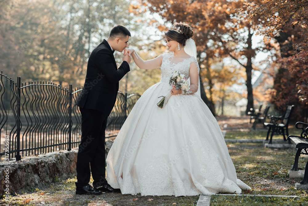 Stylish groom gently kissing hand bride's. Wedding. Stylish and beautiful. Beautiful bride with modern bouquet possing with stylish groom in autumn park. Sensual romantic moment. 