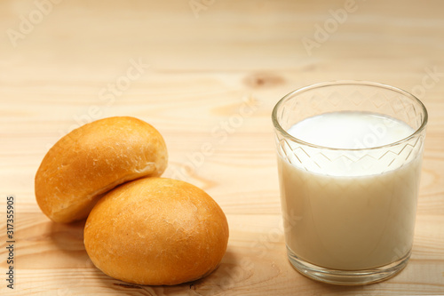 A glass of milk and two buns on a wooden background