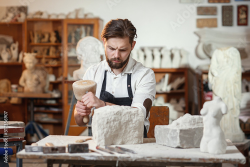 Stone carver works with wooden hammer and chisel at limestone. photo