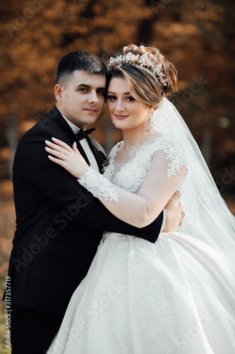 Autumn wedding. Close-up of newlyweds smiling and caressing. Loving wedding couple. Lovely young couple in love glow with happiness together. Newlyweds smile at each other at wedding day. © Tetiana Moish