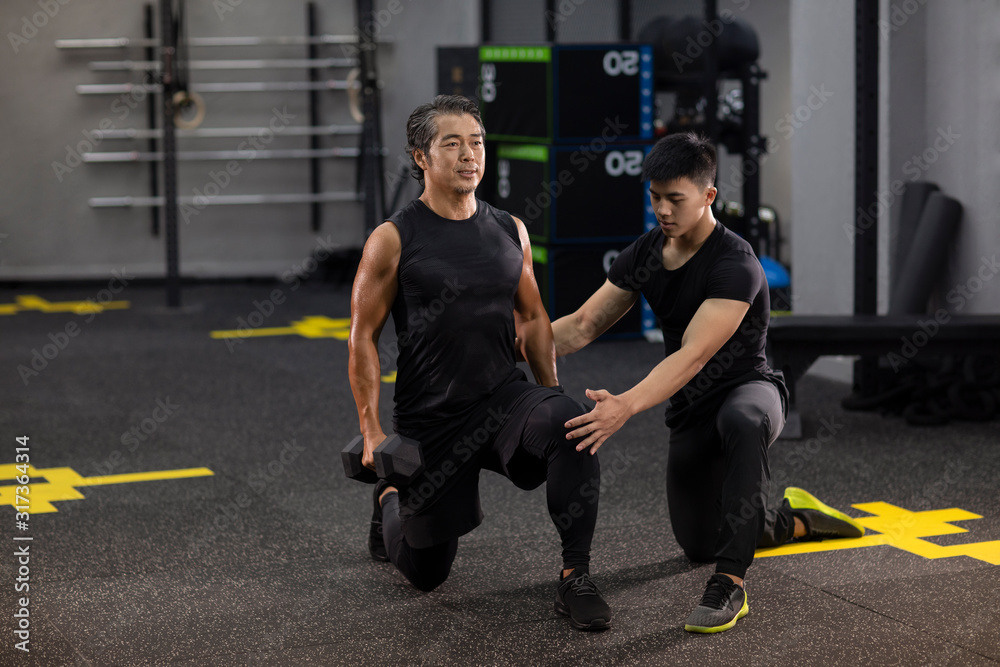 Mature man working out with personal trainer at gym