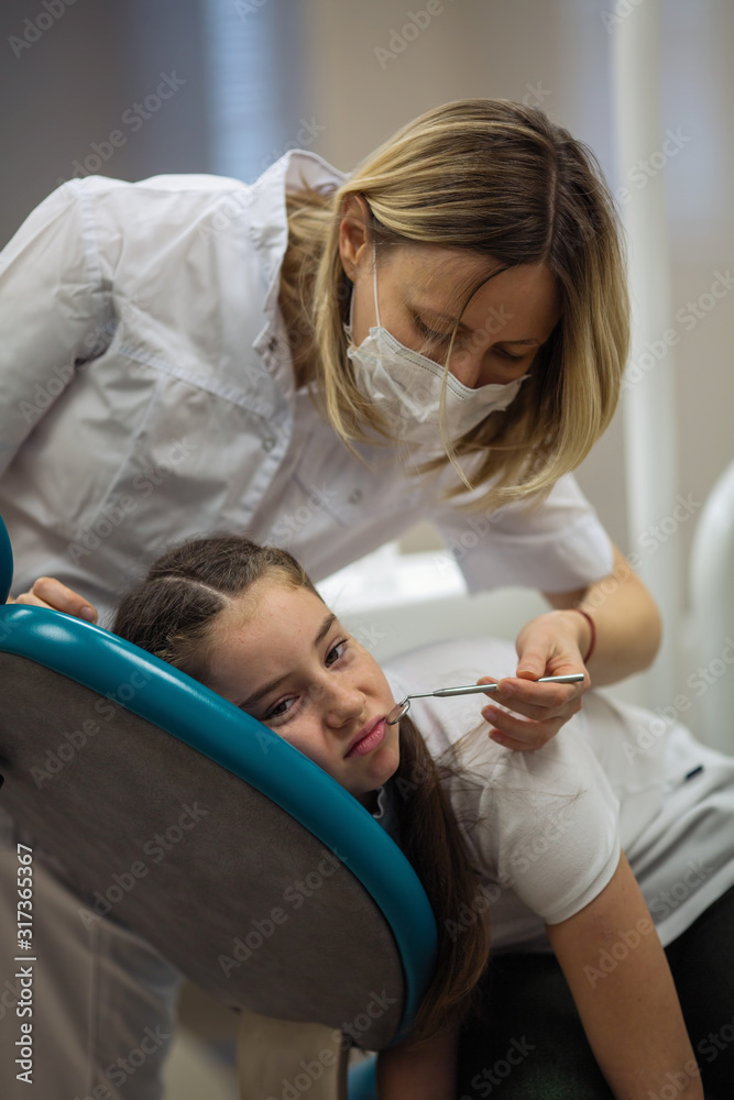 Dentist doing teeth checkup of little girl looking afraid and sad in a