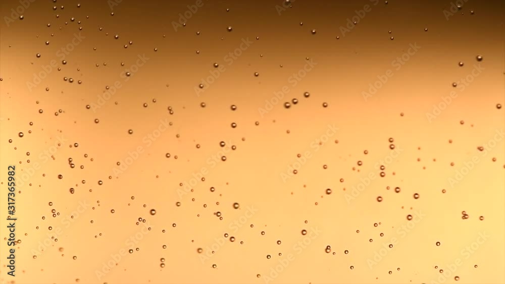 Champagne bubbles background close-up. Macro shot of sparkling wine gold backdrop. Bubbly fizzing sparkling wine closeup. Beer. Holiday celebrating. Slow motion 4K UHD video