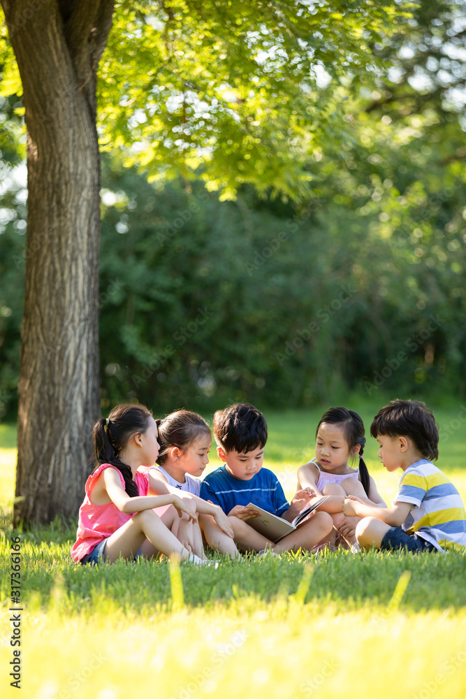 Happy children reading book on meadow Happy children reading book on meadow