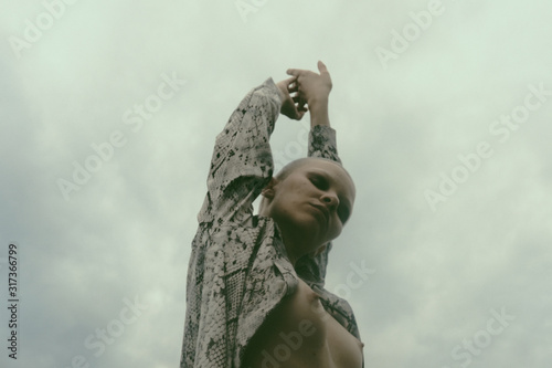 Stylish bald woman with bare breast against cloudy sky photo