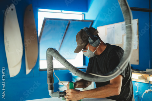 Worker in protective mask adjusting details surfboard in workshop photo