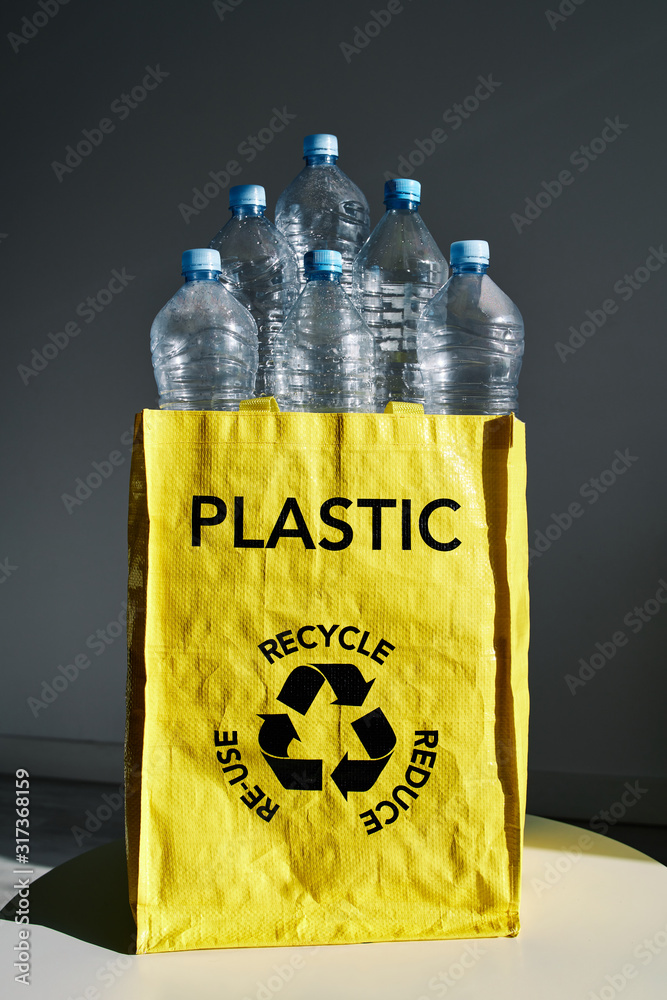 Heap of empty water bottles in yellow bag with recycle sign on gray