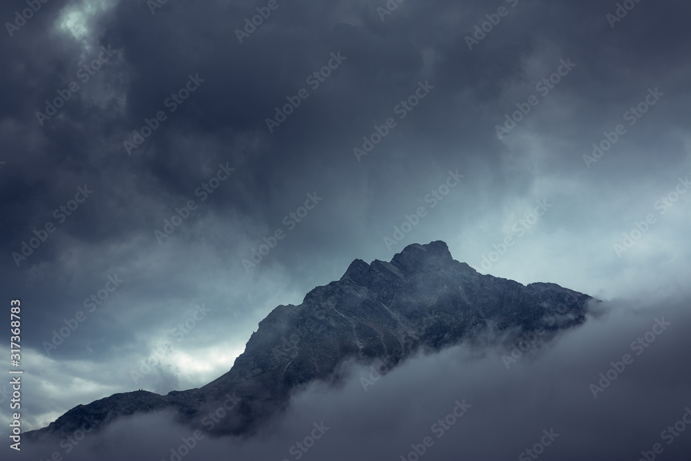 Dramatic mysterious rocky peak under gray clouds in foggy mist in Austria Dramatic mysterious rocky peak under gray clouds in foggy mist in Austria