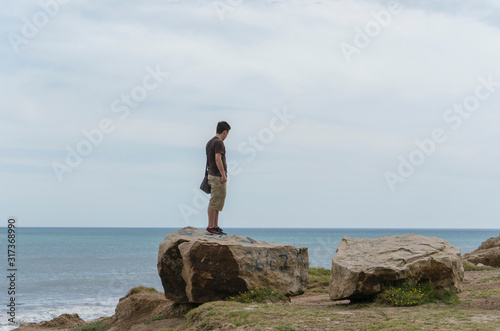 Young man standing on a rock looking at the sea