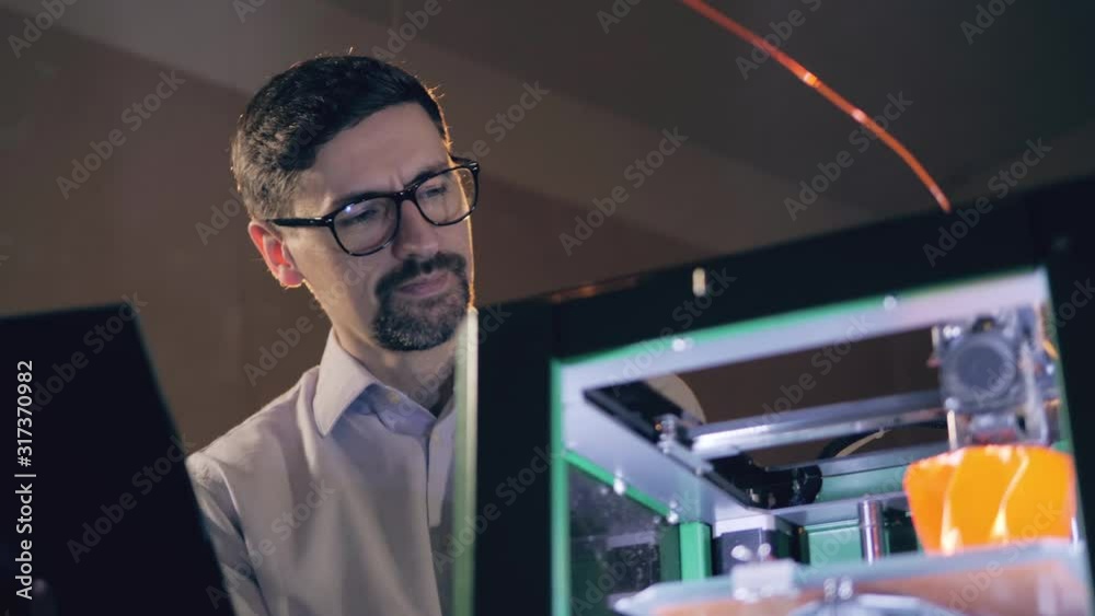 An engineer with a laptop is watching 3D-printer at work An engineer with a laptop is watching 3D-printer at work
