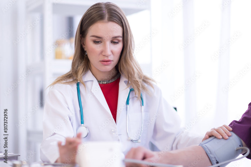 A female doctor wearing a white coat with a stethoscope is checking the blood pressure of the patient. A female doctor wearing a white coat with a stethoscope is checking the blood pressure of the patient.