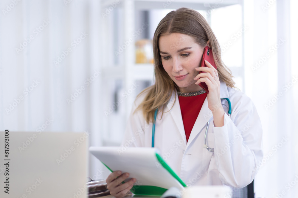 A female doctor wearing a white coat talking on the phone with a patient A female doctor wearing a white coat talking on the phone with a patient