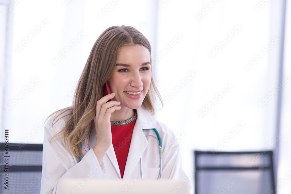 A female doctor wearing a white coat talking on the phone with a patient A female doctor wearing a white coat talking on the phone with a patient
