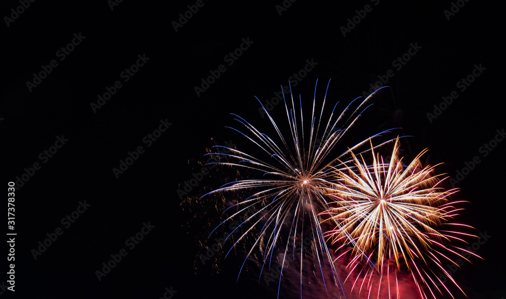 Blue-tipped white starburst firework beside a white starburst firework with red highlights against a black background