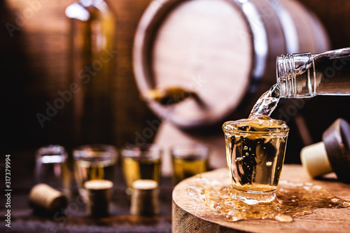 Glass of golden rum, with bottle. Bottle pouring alcohol into a small glass. Brazilian export type drink. Brazilian product for export, distilled drink known as brandy or pinga. Day of cachaça. photo