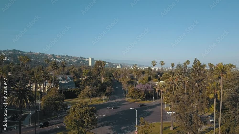 Ground to Aerial View of Beautiful Beverly Hills California with Green Palm Trees, Hollywood Hills, Mountains, and Traffic Crossing Intersection Los Angeles California Sunset Afternoon Day 4K Drone Ground to Aerial View of Beautiful Beverly Hills California with Green Palm Trees, Hollywood Hills, Mountains, and Traffic Crossing Intersection Los Angeles California Sunset Afternoon Day 4K Drone