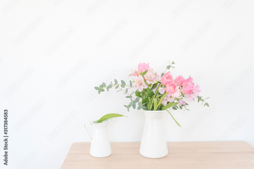 白い花瓶とピンクの花　テーブル　木製テーブル　白い壁　室内　部屋　屋内　アレンジメント　花束　花　春　ピンク　観葉植物　華やか　爽やか　春らしい　かわいい　おしゃれ　白背景　文字スペース　コピースペース　ホワイトスペース　余白　横位置