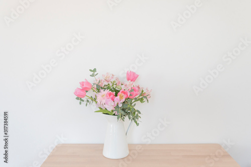 シンプルな花瓶とピンク系の花　ピンク系の花とグリーン　部屋　白壁　白背景　室内　屋内　自然光　余白　ホワイトスペース　コピースペース　文字スペース　横　背景素材　背景　グラフィック素材　　白　緑　ピンク　春　季節　スイートピー