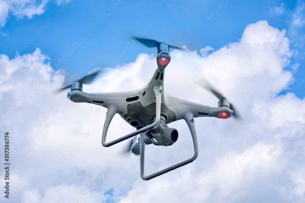 White drone quadcopter taking off from the ground on background of blue sky. White drone quadcopter taking off from the ground on background of blue sky.