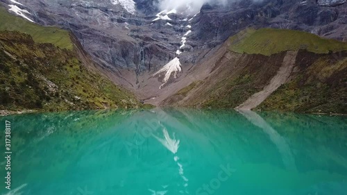 Aerial, tilt up, drone shot over turquoise glacial lagoon, the Humantay lake, in the Andes mountains, on a cloudy day, near Cusco, Peru, South America photo