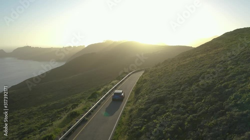 Car driving along the winding coastal roads of the Marin Headlands in San Fransisco, California, at sunset. Aerial follow shot photo