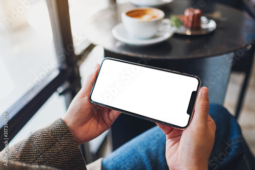 Mockup image of a woman holding black mobile phone with blank desktop screen while sitting in cafe photo