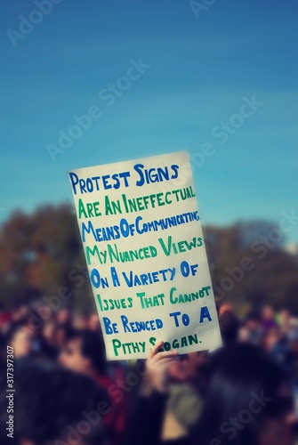 A person, in a large crowd, holding sign about protest signs; how views need a nuance conversion vs. a catchy chant. photo