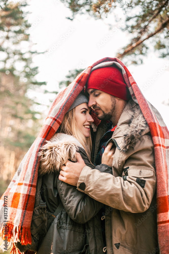 Couple huggings travelers covered with plaid in the forest. Concept of trekking, adventure and seasonal vacation. Couple huggings travelers covered with plaid in the forest. Concept of trekking, adventure and seasonal vacation.
