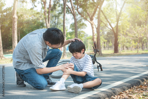Young asian father of dad calms son that fell from the bike and he get injury on knee and leg while have weekend leisure in public park,accident can happen everywhere and every time.