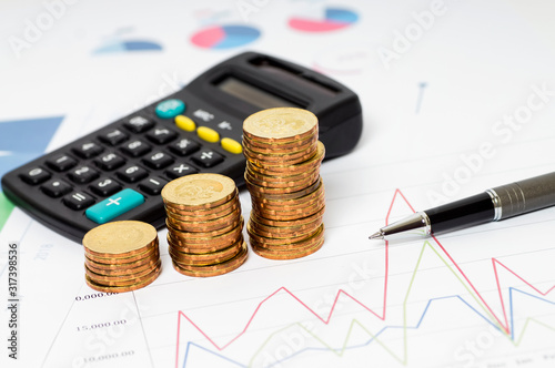 Business and Finance Concept: Stacked gold coins, calculator, pen on graphic chart