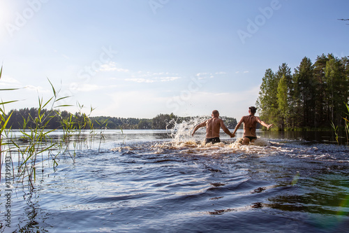 Bild auf Leinwand Man and a woman hold hands, swim and have fun in a clear forest lake on a hot summer day