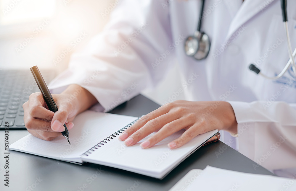 Cropped shot of female doctor writing recipe on notebook while working at office desk in hospital. Cropped shot of female doctor writing recipe on notebook while working at office desk in hospital.