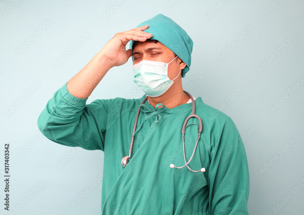 male asia surgeon sad ,surgeon showing stethoscope wearing surgeon mask , on a blue background in studio. male asia surgeon sad ,surgeon showing stethoscope wearing surgeon mask , on a blue background in studio.