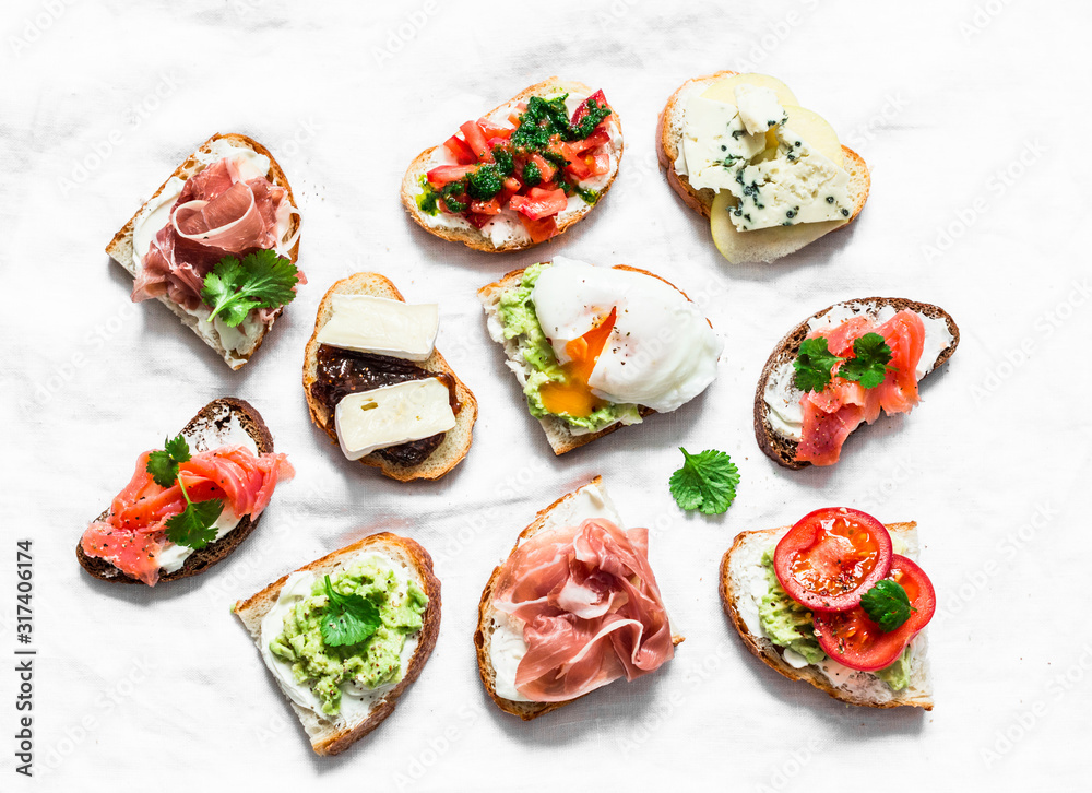 Variety of tapas sandwiches - sandwiches with prosciutto, avocado, salmon, egg, tomatoes, jamon, gorgonzola, brie, pear on a light background, top view. Delicious snack, appetizers Variety of tapas sandwiches - sandwiches with prosciutto, avocado, salmon, egg, tomatoes, jamon, gorgonzola, brie, pear on a light background, top view. Delicious snack, appetizers