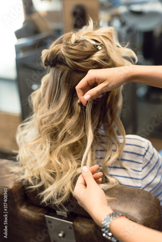 The hairdresser creates curls and wavy hair in the blonde. Hands of the hairdresser curls curls at the client