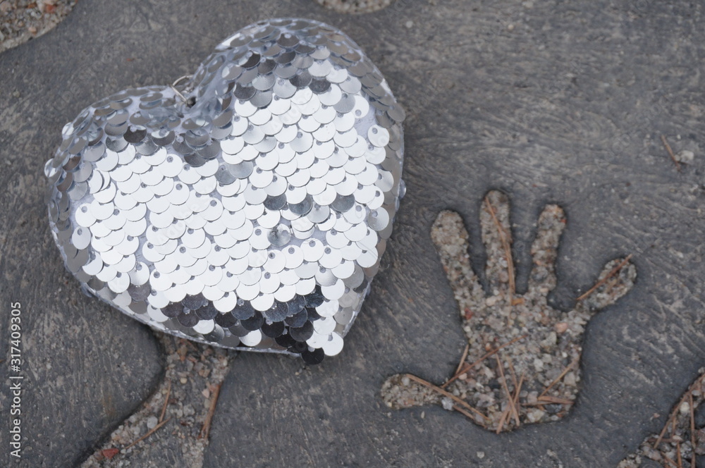 Obraz premium Silver heart on concrete background and trace of a child’s hand, concept of love and peace