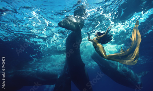 Brunette girl in Mermaid suit diving with whales in blue ocean water