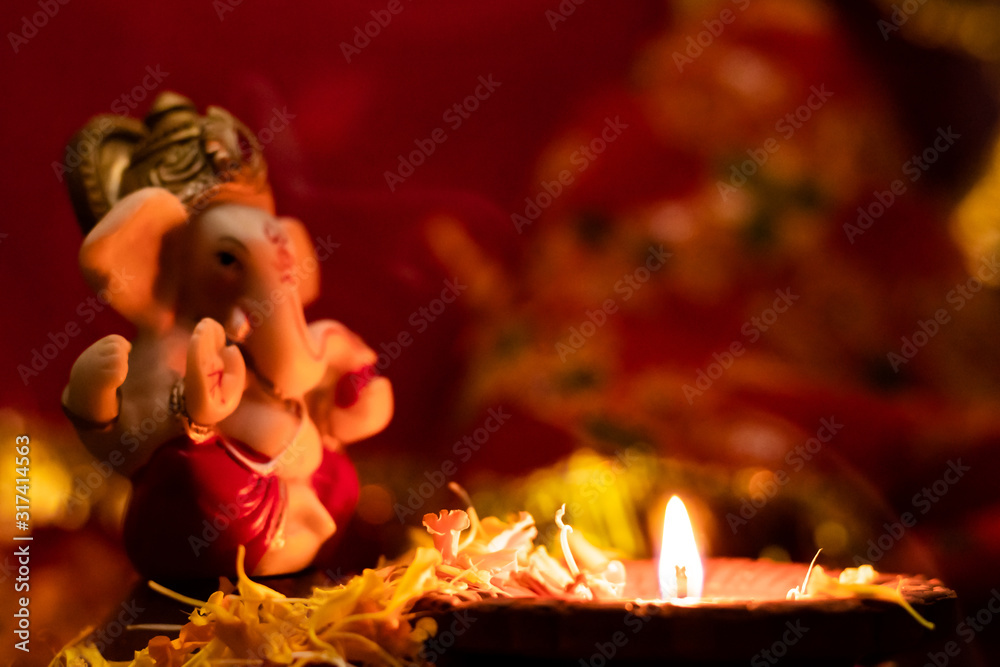 glowing diya on flower petals with defocused ganesha statue against blurry background. hinduism and faith concept.