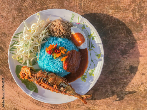 Nasi kerabu traditional in Malaysia food over the table. Its blue color. Use coconut which has been fried and mixed with rice. a combination of vegetables, duck eggs and side dishes photo